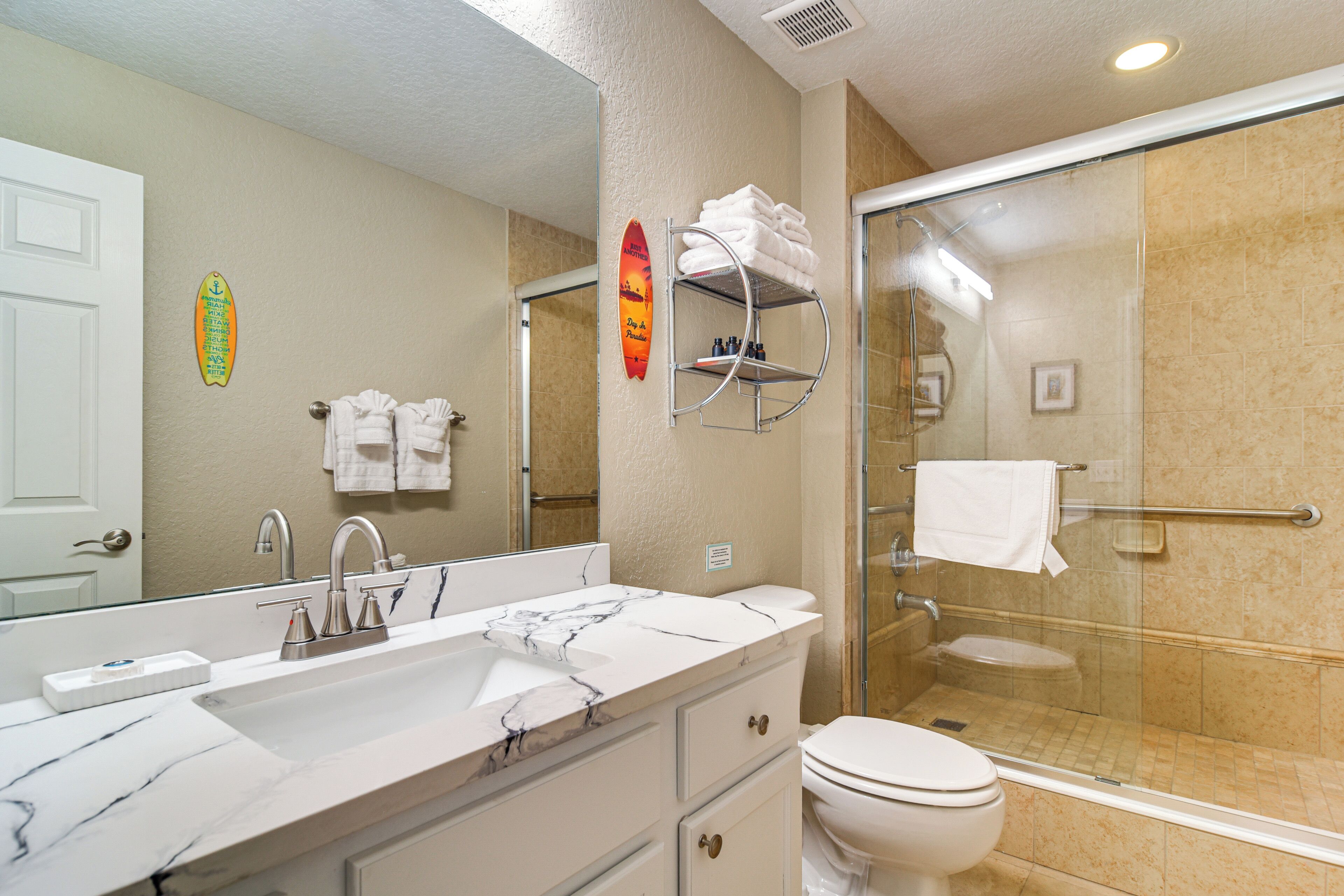 A bathroom with a marble sink, a toilet, a glass shower enclosure, and a towel rack with folded towels.