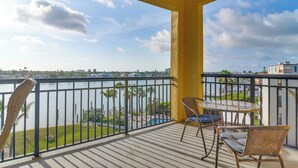 A balcony with a view of a body of water, palm trees, and a distant cityscape.