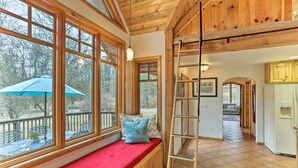 A wooden cabin interior with a red bench by large windows, a ladder, and a kitchen area. - Peaceful Shasta Cascade Getaway on 15-acre Ranch! (Weaverville)