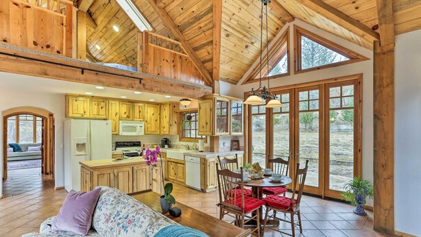 A spacious living area with a wooden ceiling, a dining table with chairs, and a kitchen area with wooden cabinets and a large window. - Peaceful Shasta Cascade Getaway on 15-acre Ranch! (Weaverville)