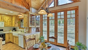 A kitchen with wooden cabinets, a dining table set with bowls and a centerpiece, and large windows offering a view of the outdoors. - Peaceful Shasta Cascade Getaway on 15-acre Ranch! (Weaverville)