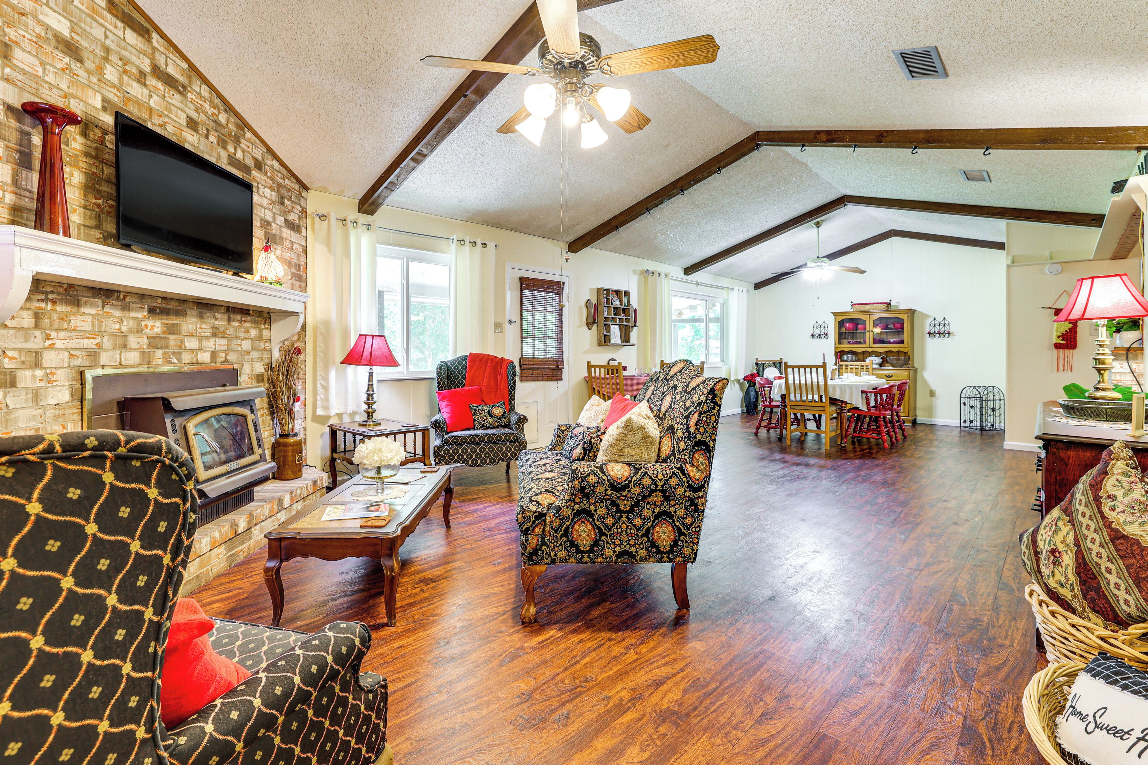 A spacious living room with hardwood floors, a fireplace, a television, and a ceiling fan.