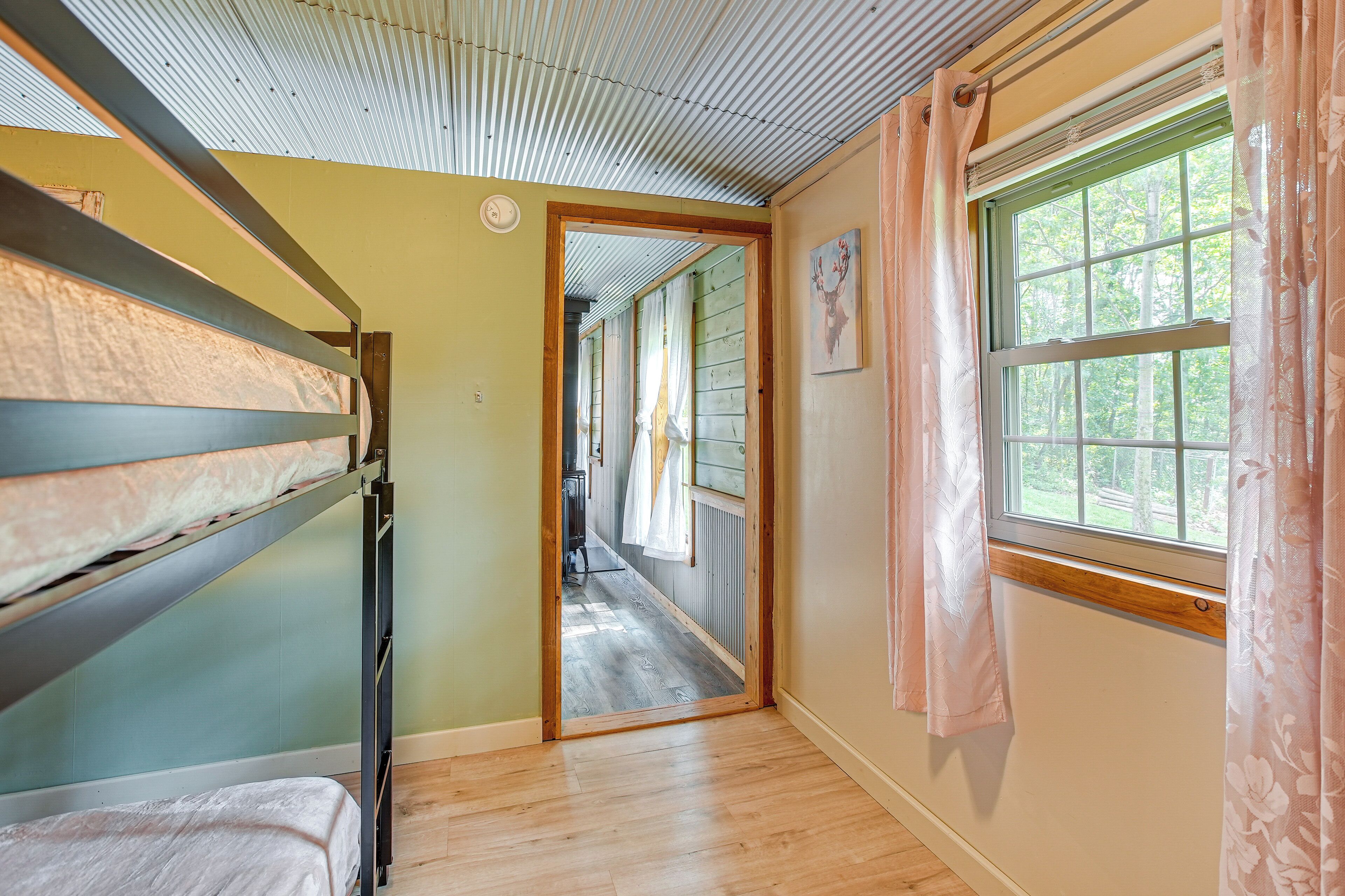 A room with bunk beds, a wooden floor, a window with curtains, and a door leading to another room.