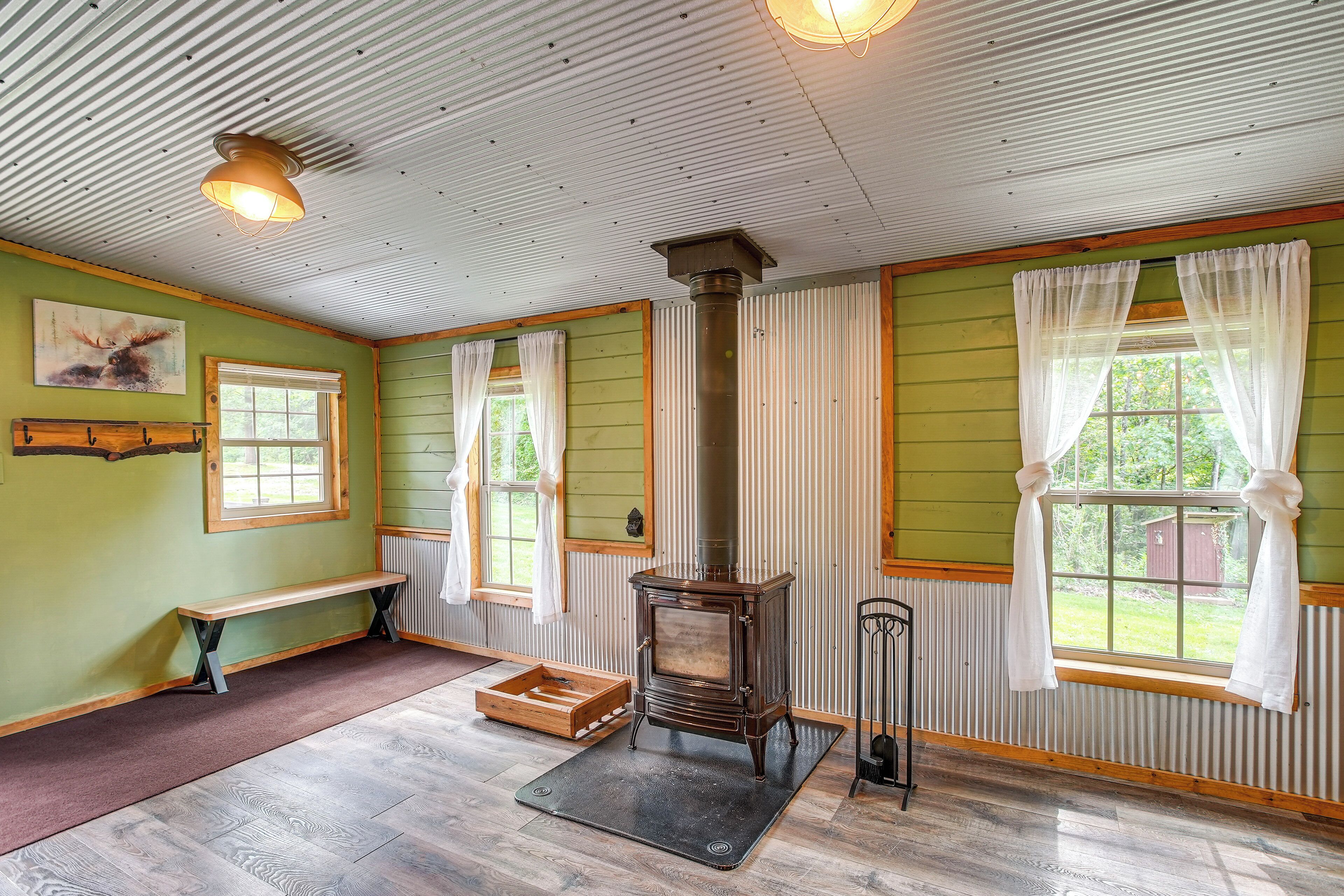 A room with a wood-burning stove, a bench, and a window with curtains.