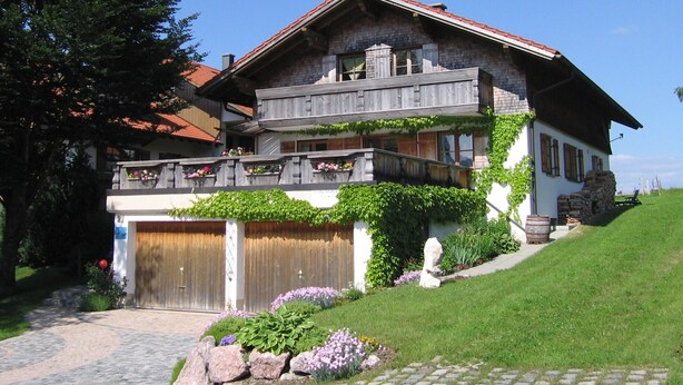 Une maison à deux étages avec un balcon en bois, une façade en pierre et une allée pavée.
