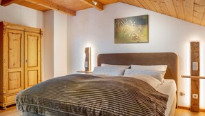 Une chambre avec un plafond en bois, un lit recouvert d’une couverture à rayures, une armoire en bois et un luminaire fixé au mur.