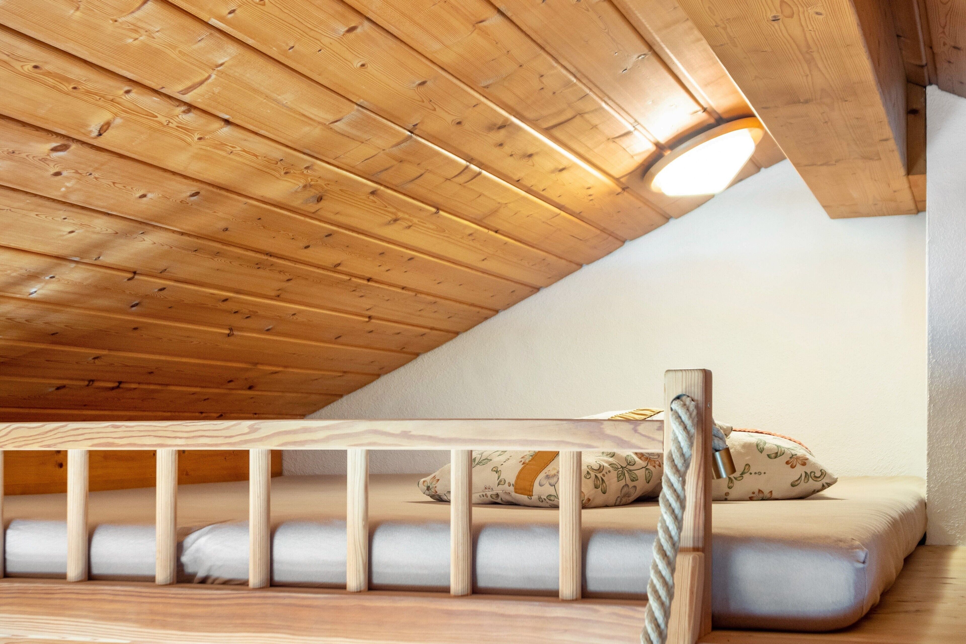 A wooden ceiling with a sloped design, a bunk bed with a pillow, and a rope ladder.