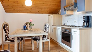Un plafond en bois, une table à manger avec des chaises, une cuisine équipée d’une cuisinière et d’un four, et une machine à café.