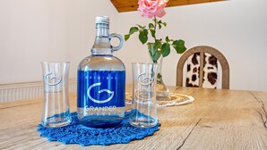 Une table en bois sur laquelle se trouvent une bouteille bleue étiquetée « GRANDER WASSER », deux verres transparents et un vase contenant une rose rose.