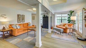 A spacious living room with two orange sofas, a coffee table, and a rug. There are large windows and a plant in the corner. - Fire Pit + Ping-pong: Home on Guadalupe River! (Seguin)