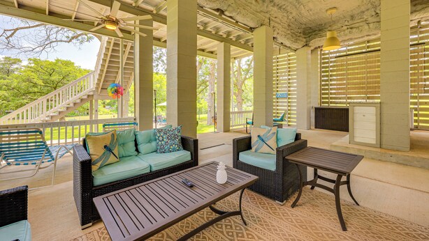 An outdoor covered patio with wicker furniture, a staircase, and a view of greenery. - Fire Pit + Ping-pong: Home on Guadalupe River! (Seguin)