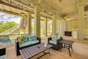 An outdoor covered patio with wicker furniture, a staircase, and a view of greenery. - Fire Pit + Ping-pong: Home on Guadalupe River! (Seguin)