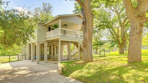 A two-story building with a balcony, surrounded by trees and a grassy area. - Fire Pit + Ping-pong: Home on Guadalupe River! (Seguin)