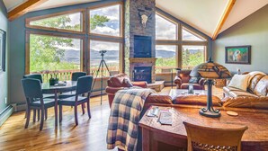 A cozy room with a stone fireplace, large windows, a dining table with chairs, and a comfortable seating area. - Private 5 Acres w/ Mtn Views: Park County Cabin! (Jefferson)
