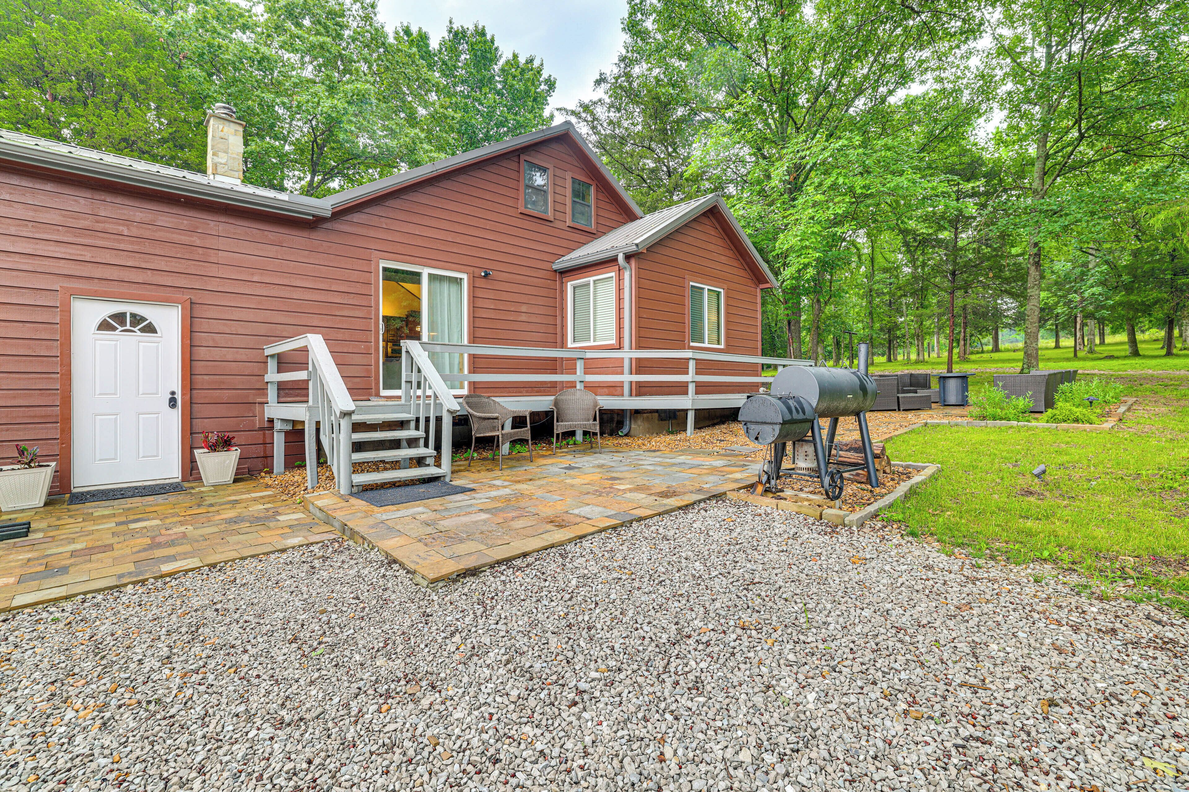 A red wooden cabin with a covered patio, outdoor seating, and a barbecue grill.