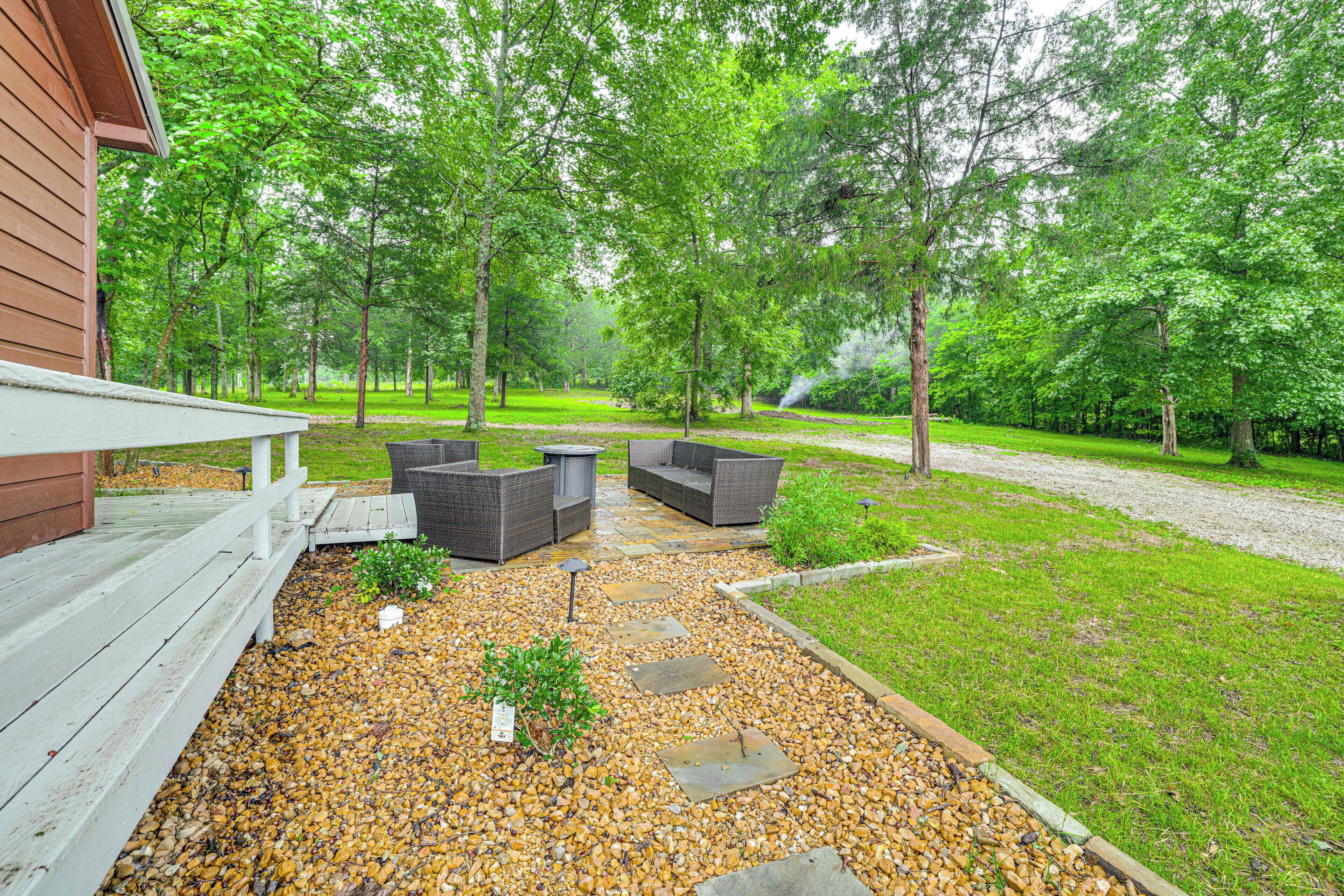 An outdoor patio with wicker furniture, a wooden deck, and a gravel pathway leading to a grassy area.