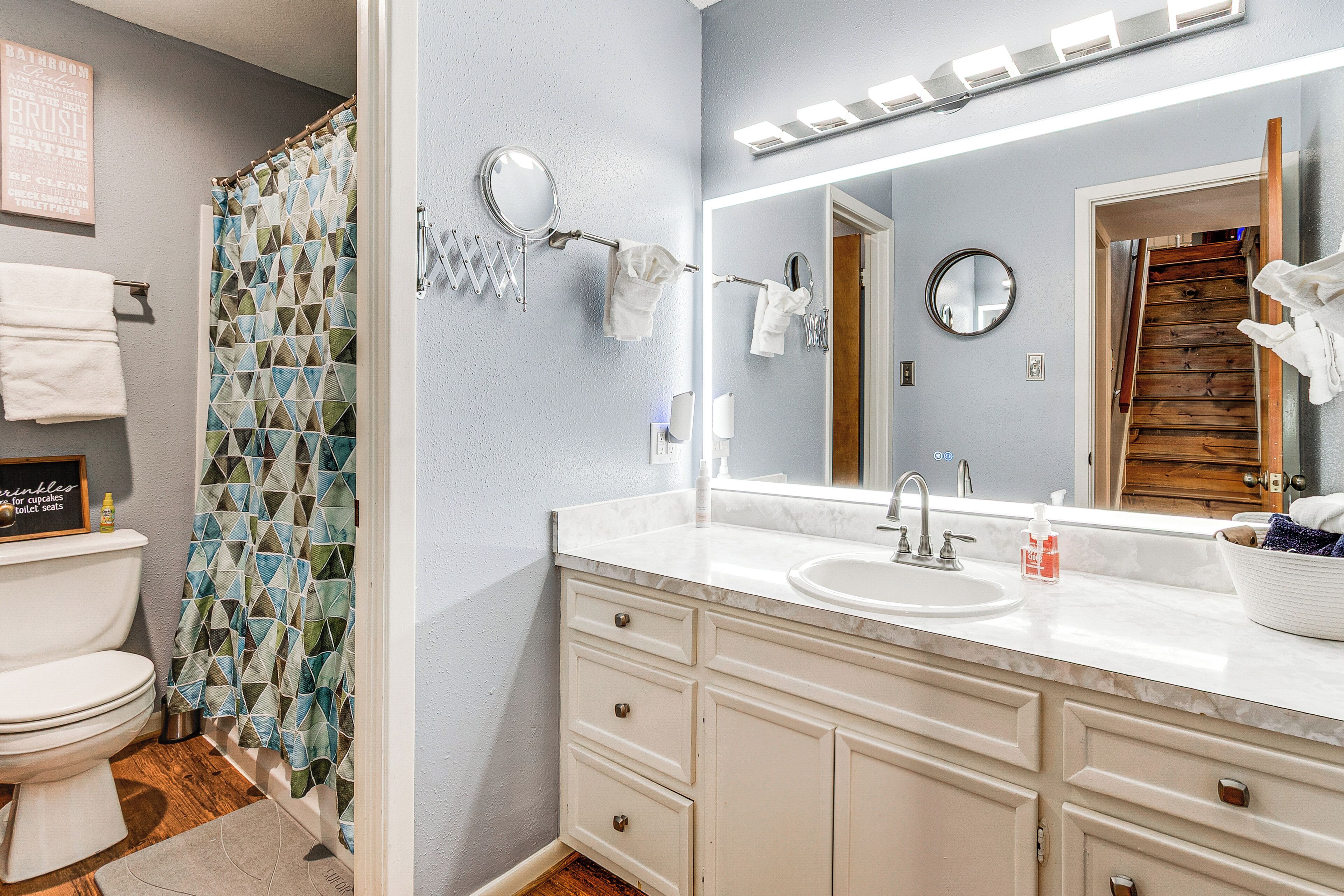 Une salle de bain avec des toilettes blanches, un lavabo avec un miroir et un rideau de douche à motifs géométriques.