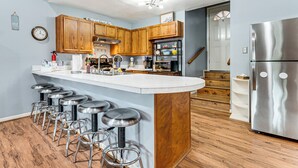 A kitchen with wooden cabinets, a stainless steel refrigerator, and a bar area with stools.