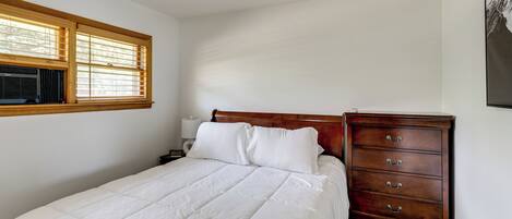 Un dormitorio con cama, cómoda de madera, mesita de noche y ventana con persianas.