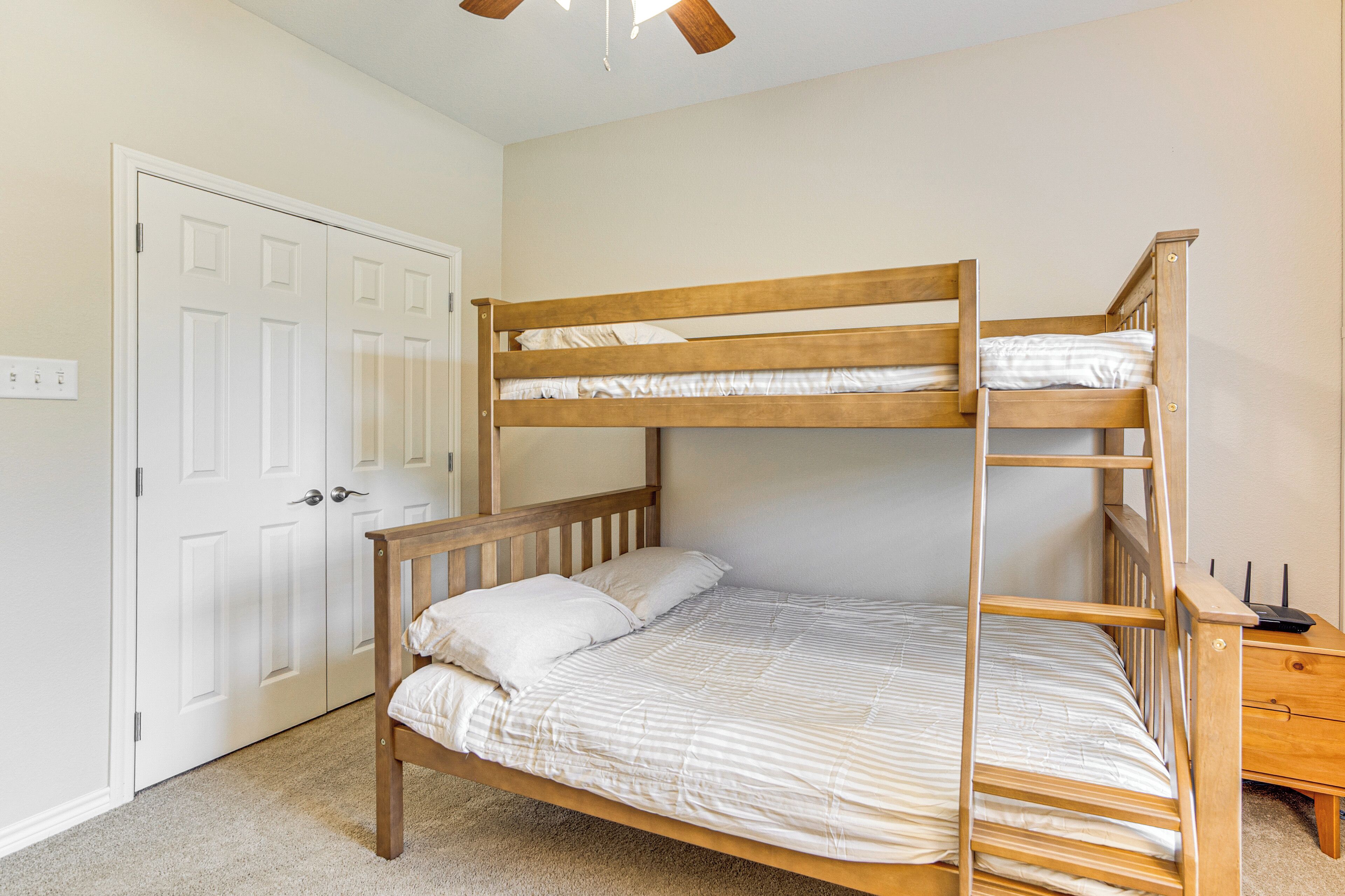 A bunk bed in a room with a white door and a small wooden nightstand.