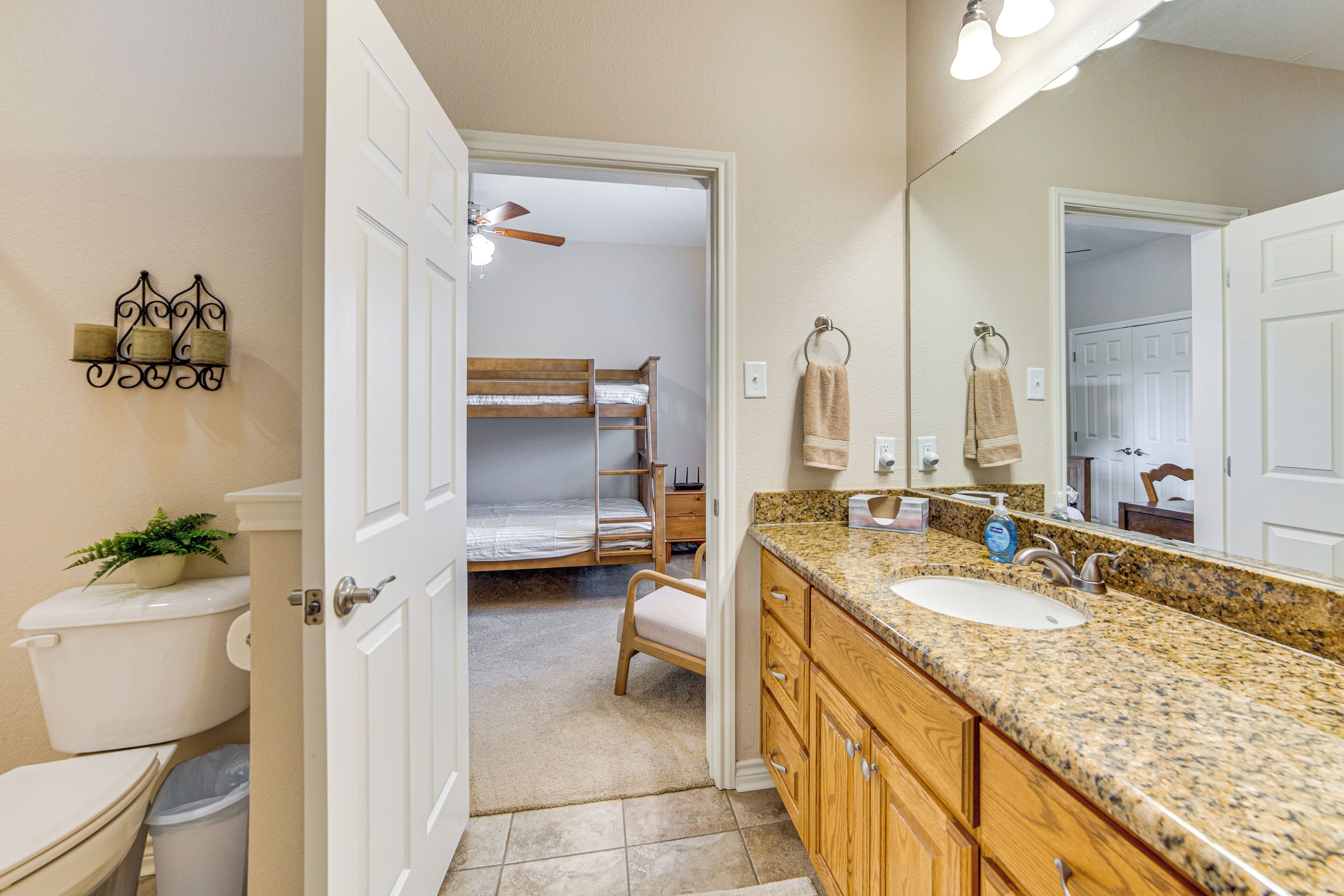 A bathroom with a sink, mirror, and a bunk bed in the adjacent room.