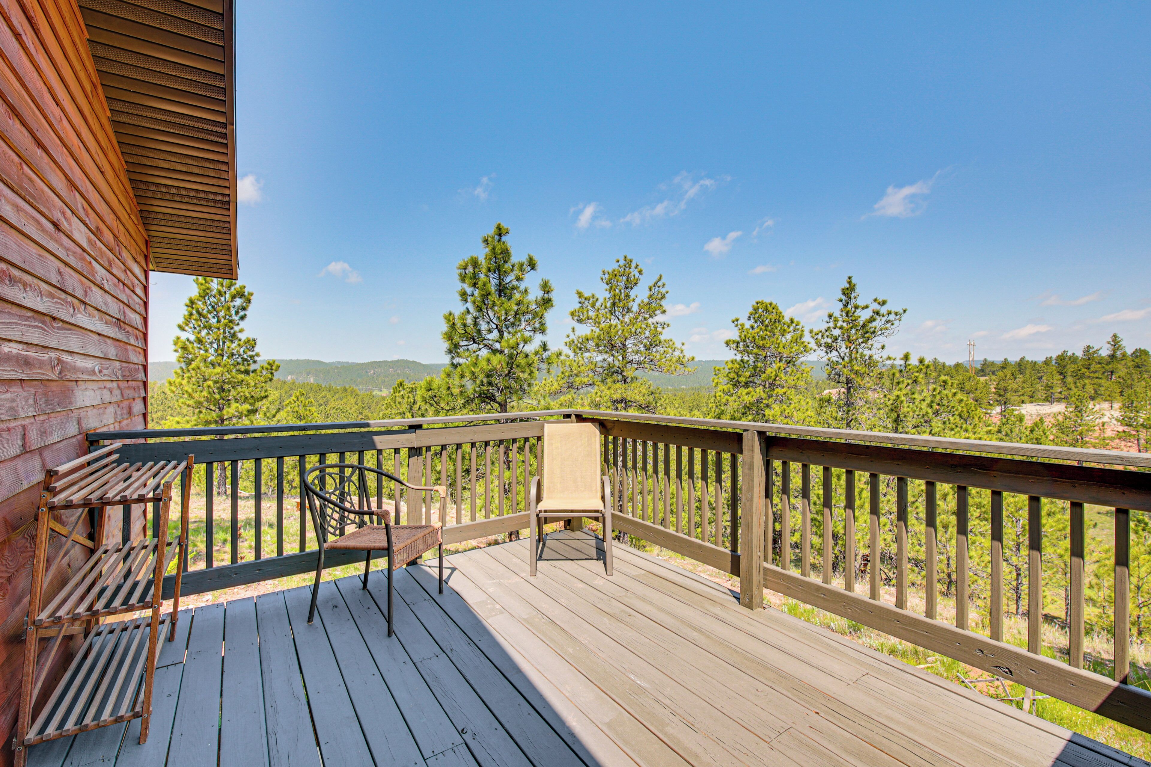 A wooden deck with a chair and a table, overlooking a forested landscape.