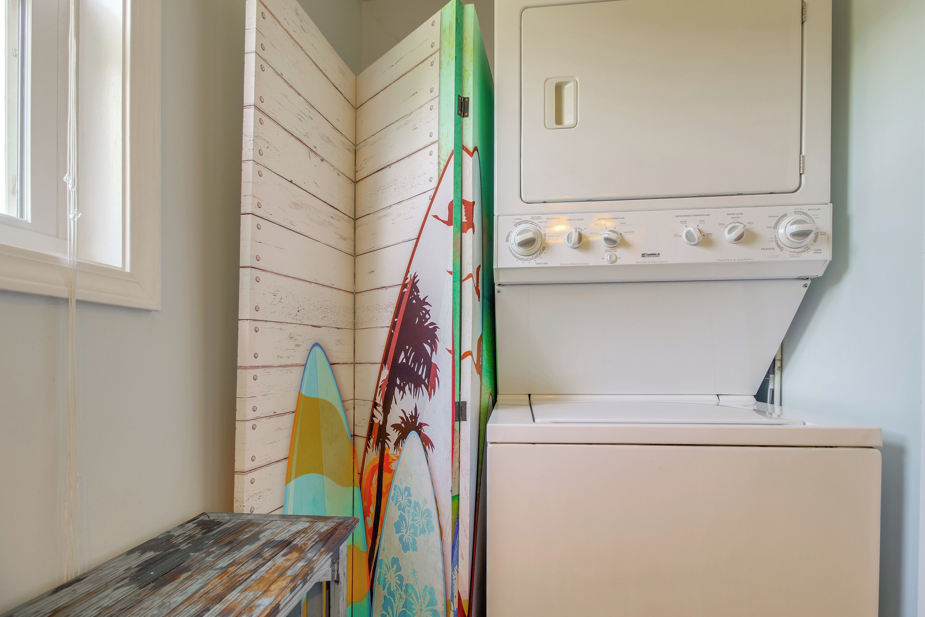 Ein Waschraum mit einer Waschmaschine und übereinander gestapelten Surfbrettern an der Wand.