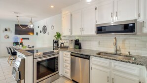 A modern kitchen with white cabinets, stainless steel appliances, a granite countertop, and a built-in oven. - Walk to North Topsail Shores: Beach House w/ Gear! (Sneads Ferry)