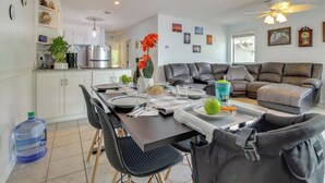 A modern living room with a brown leather sofa, a dining area with a table set for two, and a kitchen with white cabinets and stainless steel appliances. - Walk to North Topsail Shores: Beach House w/ Gear! (Sneads Ferry)