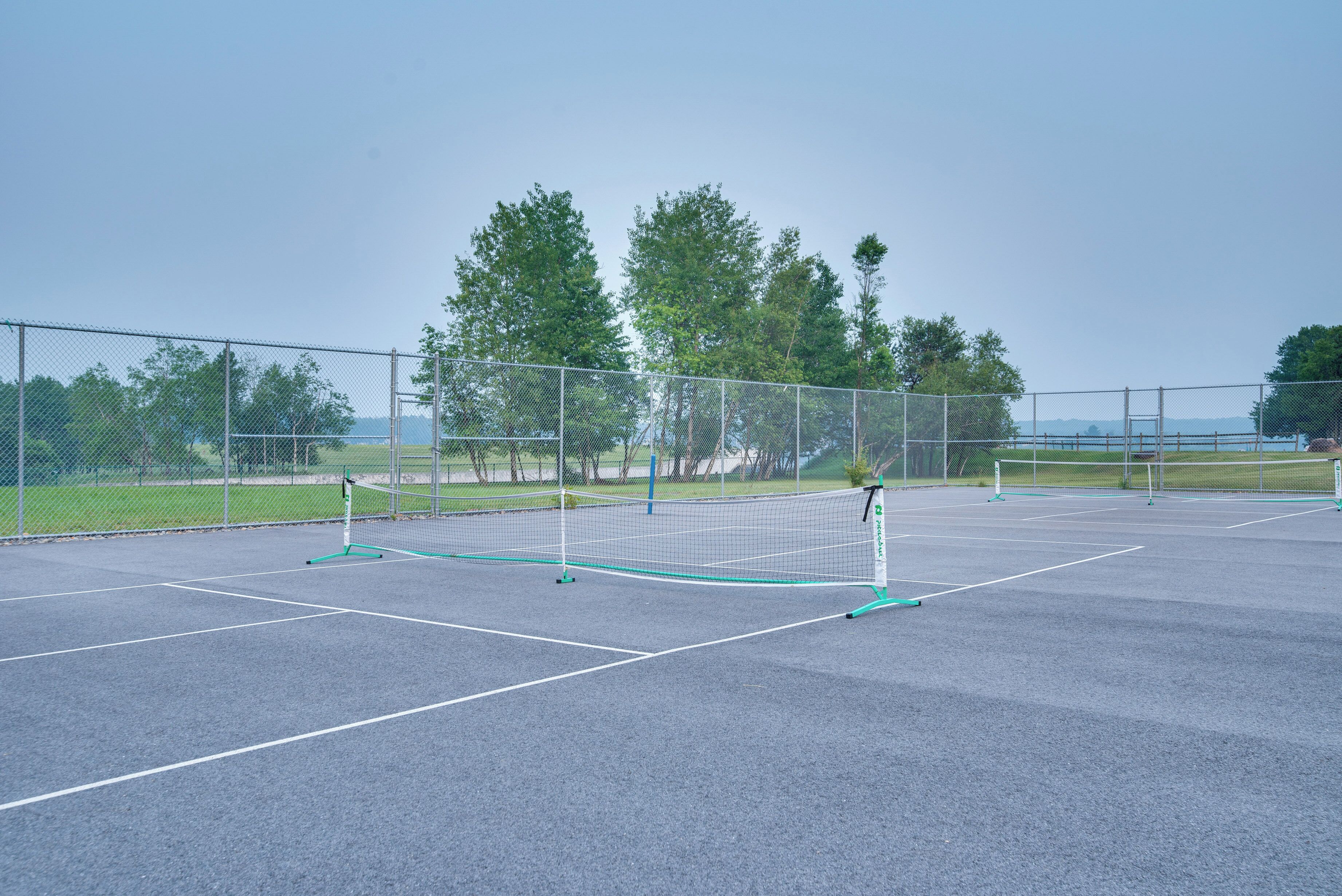 An outdoor tennis court with a net, surrounded by a fence and trees.