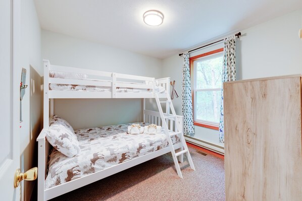 A bunk bed room with a ladder, a window with curtains, and a door with a handle.