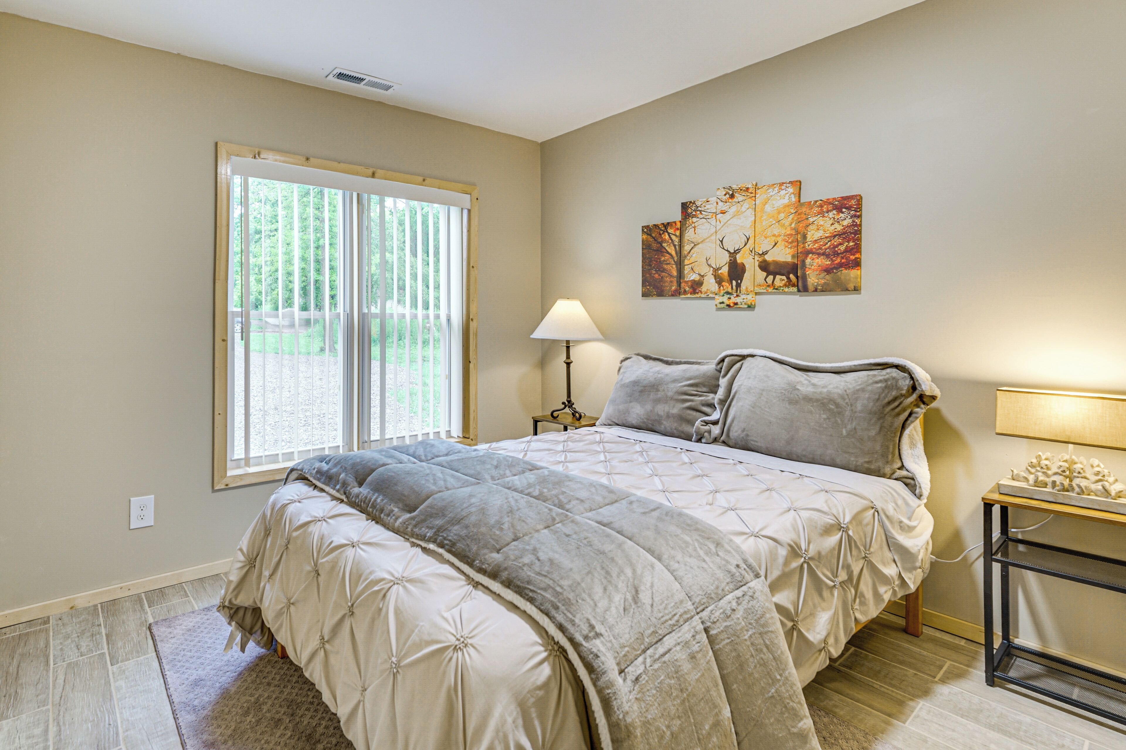 A bedroom with a large bed, a window, a lamp, and artwork on the wall.