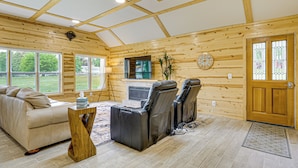 A log cabin interior with a sofa, two massage chairs, a fireplace, and large windows. - Walk to Shay Lake: Updated Home w/ Water View! (Silverwood)