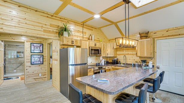 A modern kitchen with wooden walls, stainless steel appliances, and a central island with bar stools. - Walk to Shay Lake: Updated Home w/ Water View! (Silverwood)
