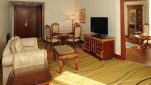 Een hotelkamer met een bank, fauteuil, houten salontafel, tv-meubel en een kamerbreed tapijt met dessin.