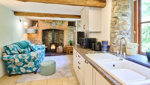 A cozy kitchen with a stone fireplace, a sofa with floral upholstery, and a sink with a compost bin. - Host Stay Dipple Farm Cottage (Bideford)
