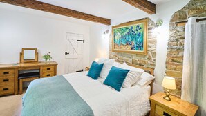 A bedroom with a bed, a nightstand, a dresser, a painting, and a stone wall. - Host Stay Dipple Farm Cottage (Bideford)