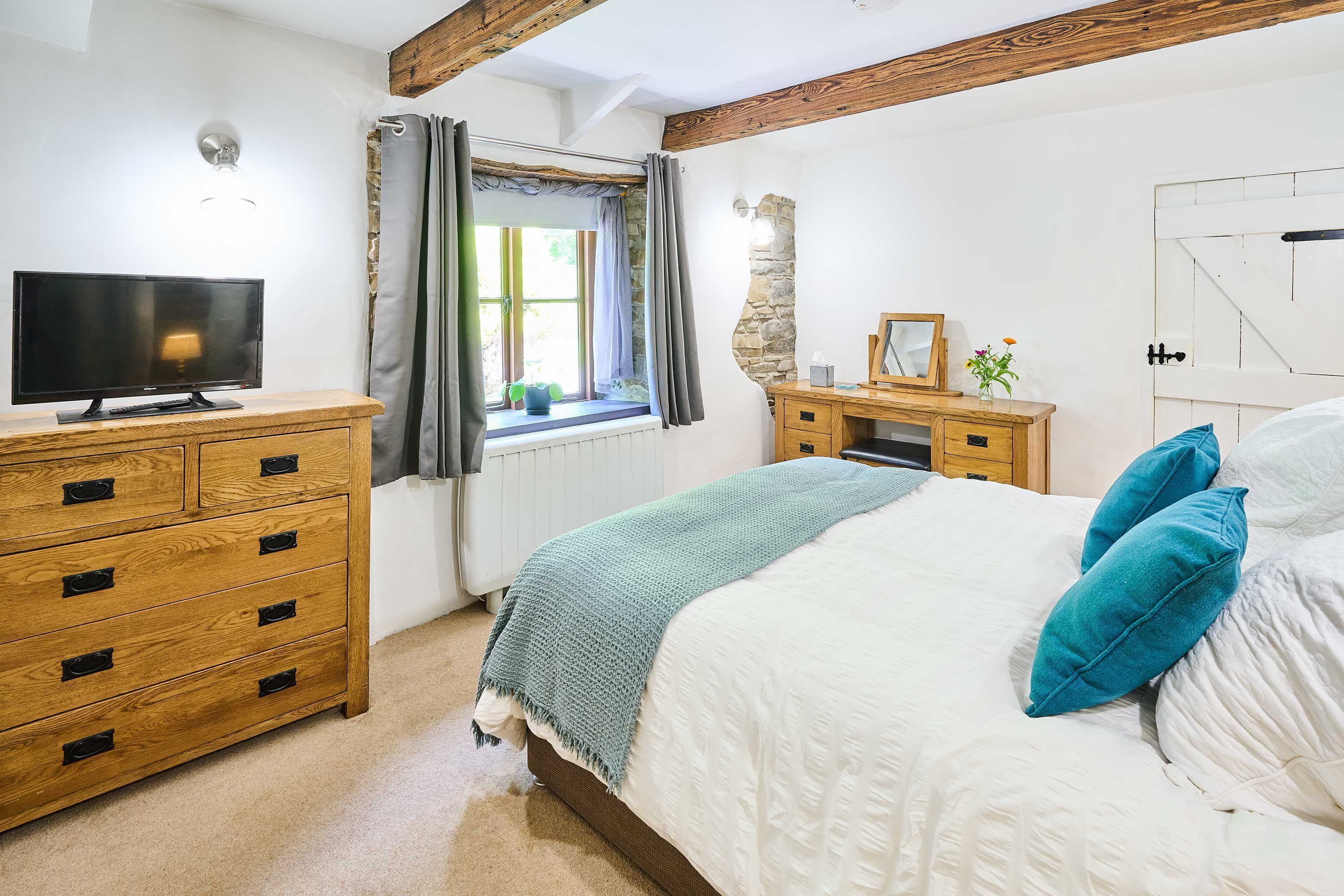 A bedroom with a bed, wooden dresser, television, and a window with curtains.