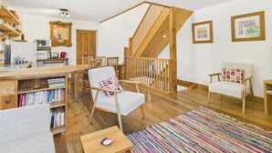 Una sala de estar acogedora con una escalera de madera, un comedor y una cocina equipada con microondas y hervidor.