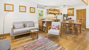 Una sala de estar acogedora con un sofá, una mesita y una silla. Hay una zona de cocina con microondas, tostadora y armarios de madera.