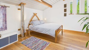 Un dormitorio con una cama de madera, un tragaluz, un radiador, un banco, una alfombra colorida y una ventana con vistas a árboles.