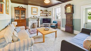Una sala de estar acogedora con un sofá, una mesa de centro de madera, una chimenea y un reloj de pie grande.