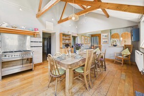 Une cuisine dotée d’un grand poêle, d’une table à manger en bois, de chaises et d’une structure de plafond en bois.