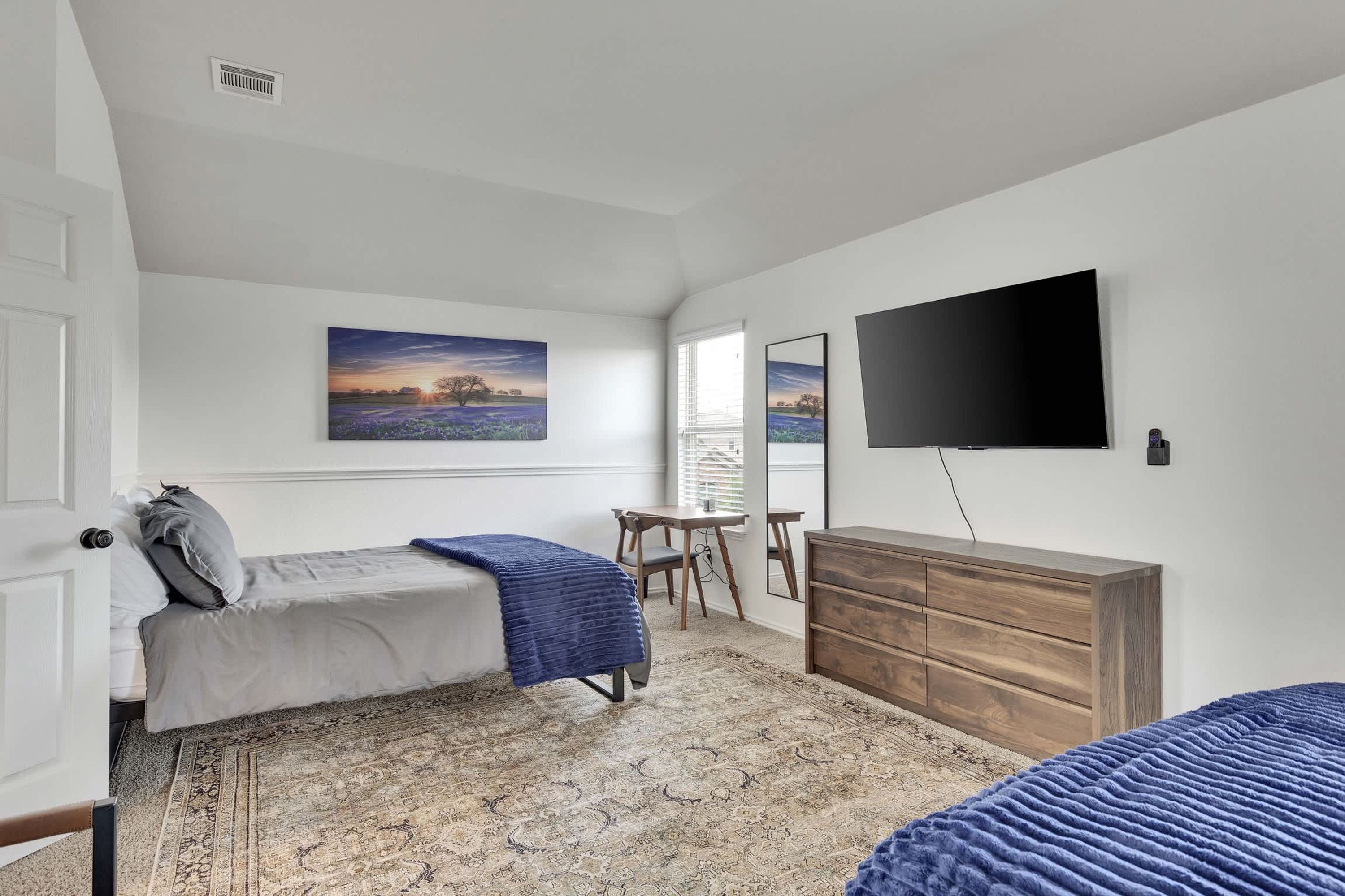Une chambre avec deux lits, un bureau, une commode et un téléviseur.