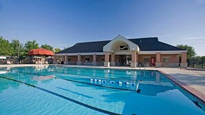 A swimming pool with clear blue water, a covered seating area, and a building with a large entrance. - Luxury 4BR 2 5BA Home EV Charger Pool Access (Buda)