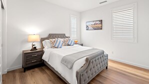 A bedroom with a bed, nightstand, lamp, and a painting on the wall. - Spacious 5BR Getaway w Game Room Modern Comfort (Fontana)