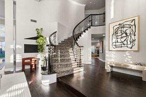 A spacious living area with a staircase, a bench, and a large abstract painting on the wall.