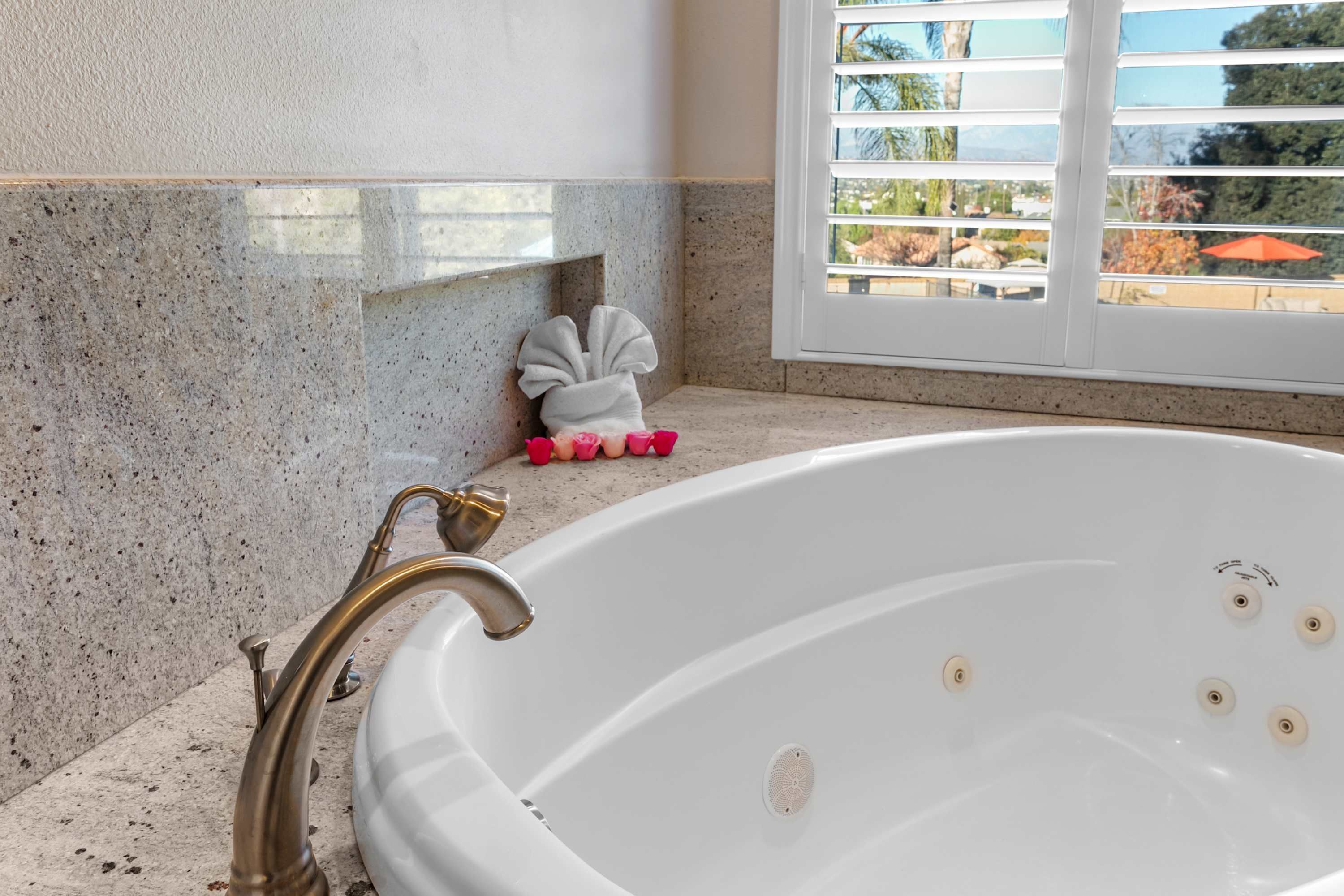 Une salle de bain dotée d’une grande baignoire blanche, d’un comptoir en granit et d’une fenêtre donnant sur l’extérieur.