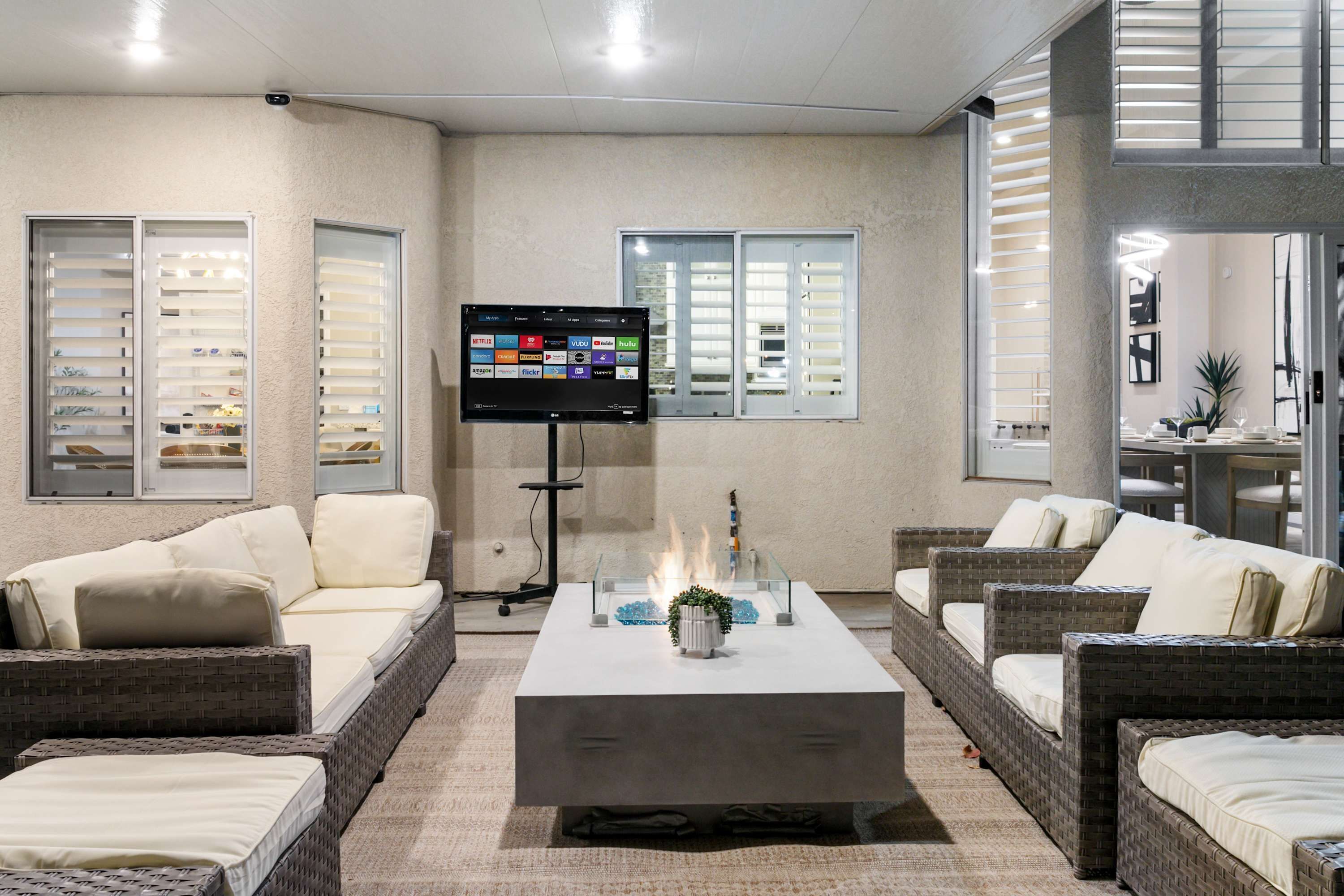 Un espace de détente moderne, avec des meubles en osier, une table basse centrale agrémentée d’une plante décorative et un téléviseur à écran plat fixé au mur.