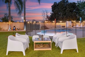 A patio area with white chairs, a glass-top table, and a small fire pit.